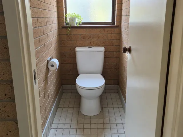 Clean white toilet in a small tiled bathroom with brick walls and a frosted window in Colyton